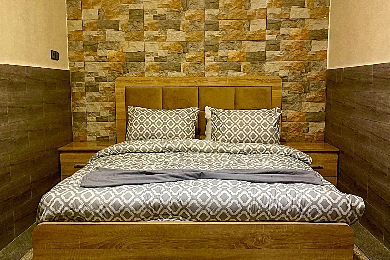 Chambre principale — lit double centré, mur d'accent en pierre et tables de chevet symétriques